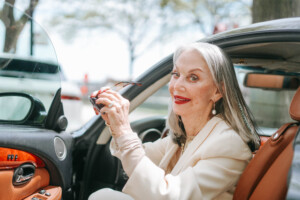 Image of Honey Good holding up her sunglasses ready to put them on stepping out of her car, smiling with red lipstick embracing serendipity