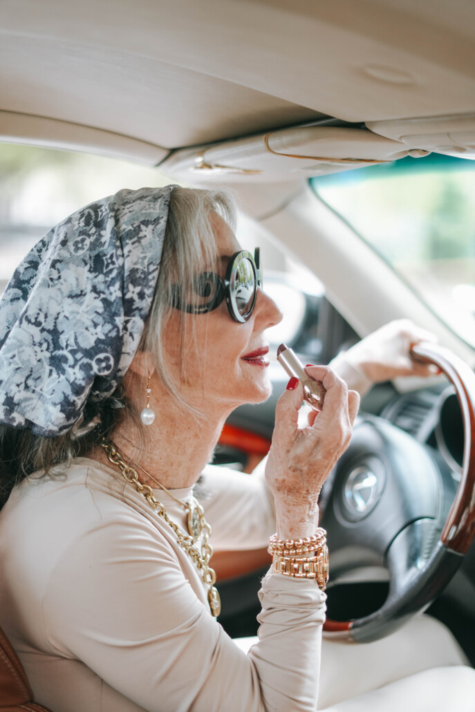 iamge on honey good in her car applying her signature red lipstick using her rearview mirror 