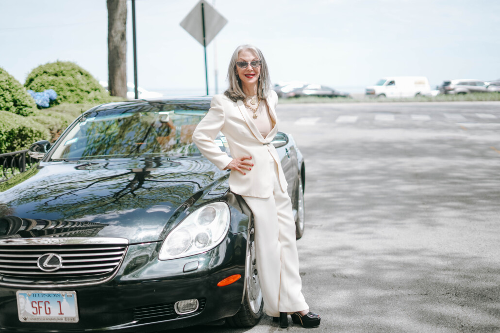 Honey Good leaning against lexus car in white suit modern grandmother